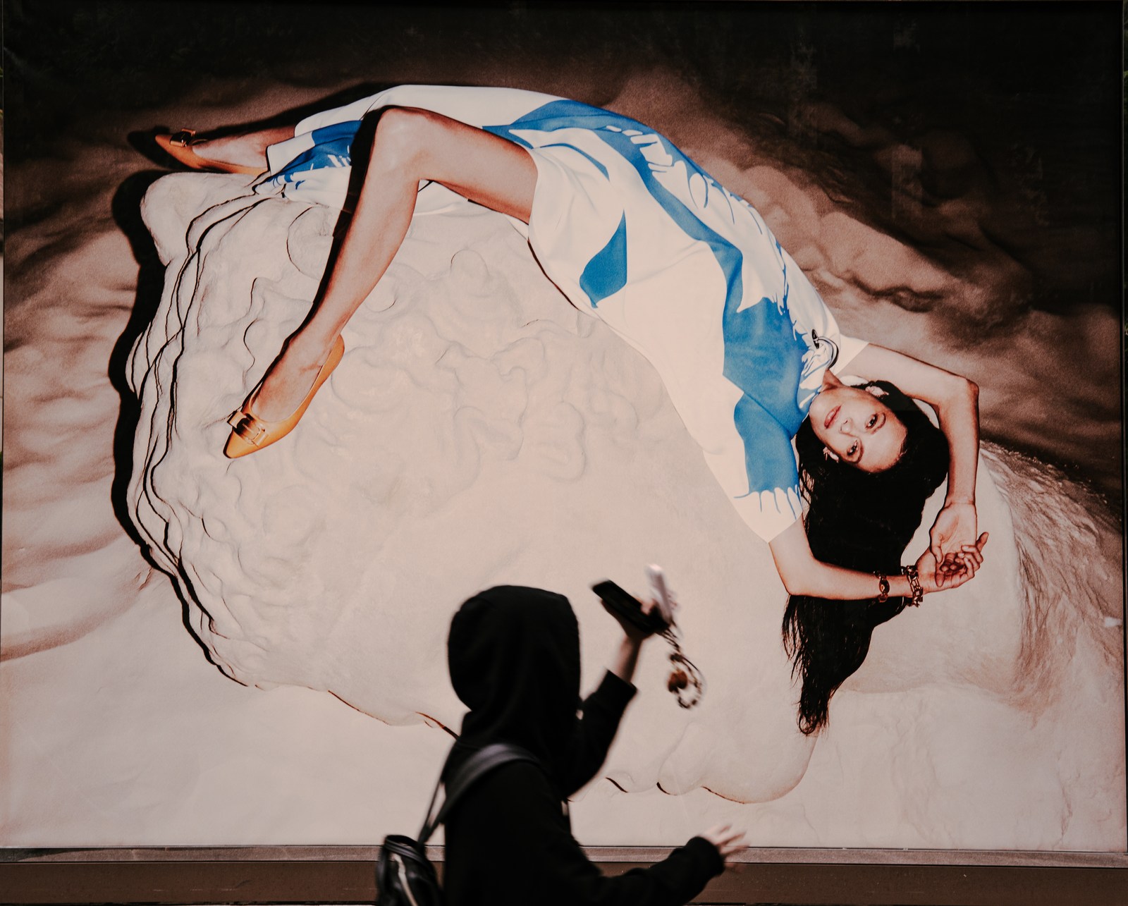 A dark passerby lifts a hand beneath a large reclining advertising figure.