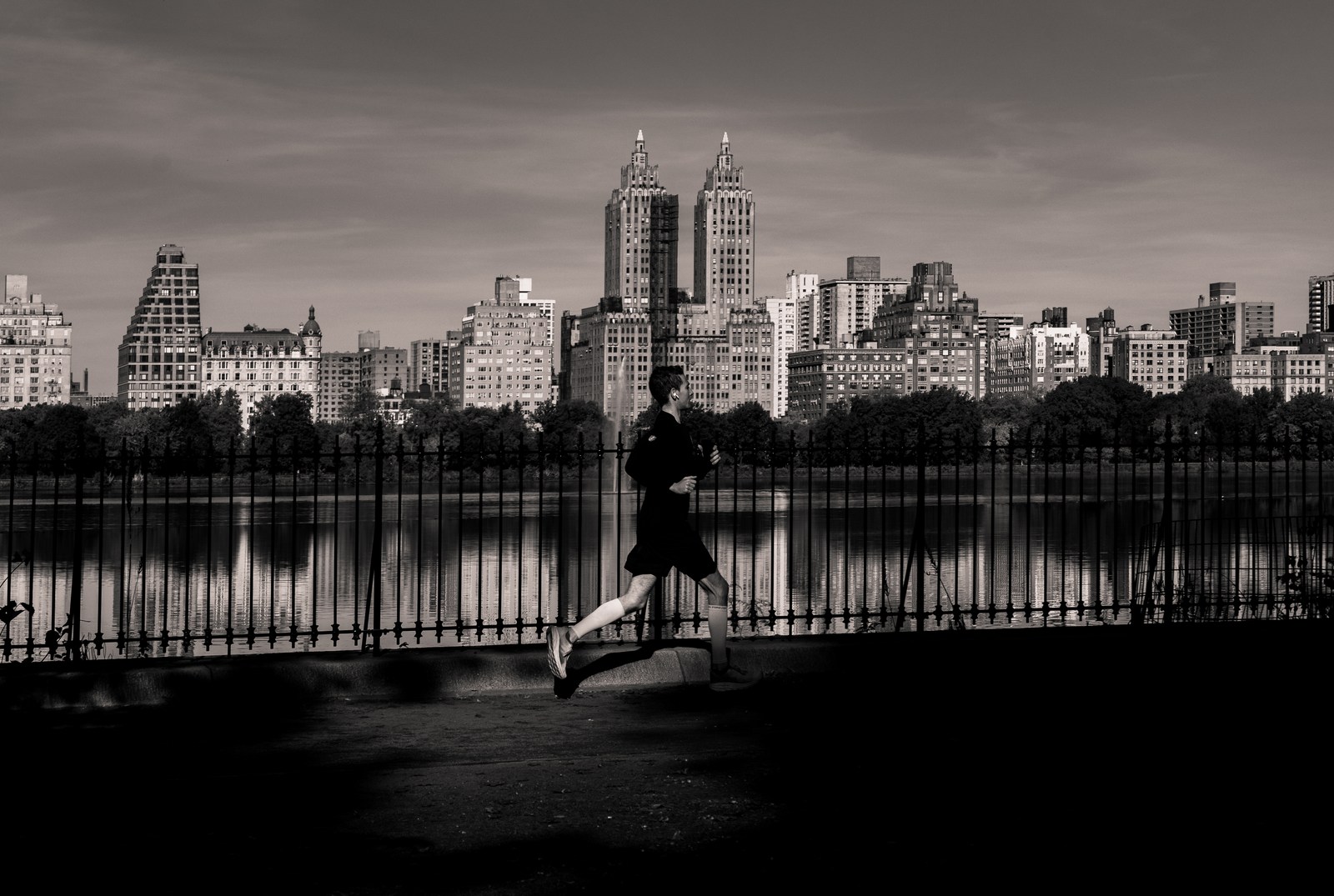 A runner is briefly airborne beside a railing and a distant monochrome skyline.