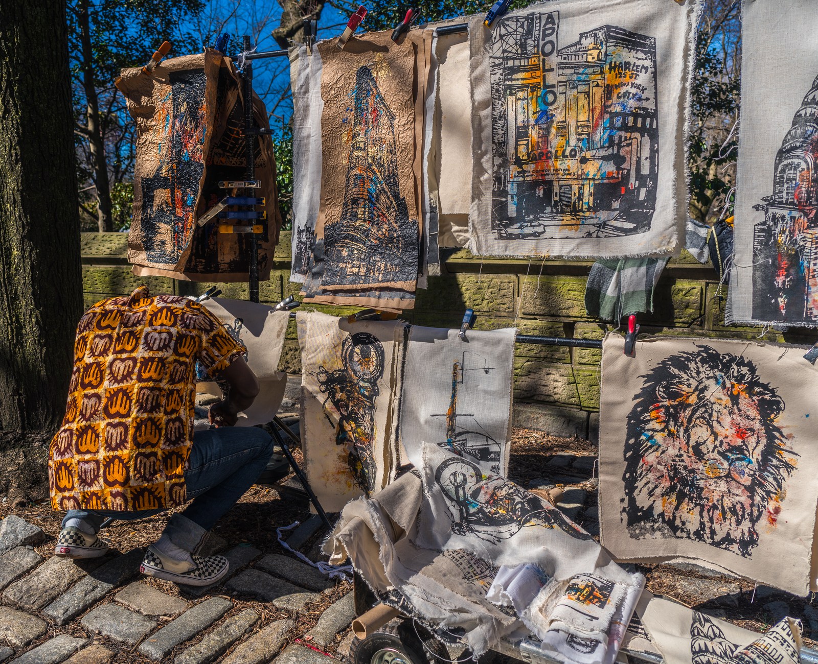 A crouched figure nearly disappears among patterned cloth and hanging pictures.