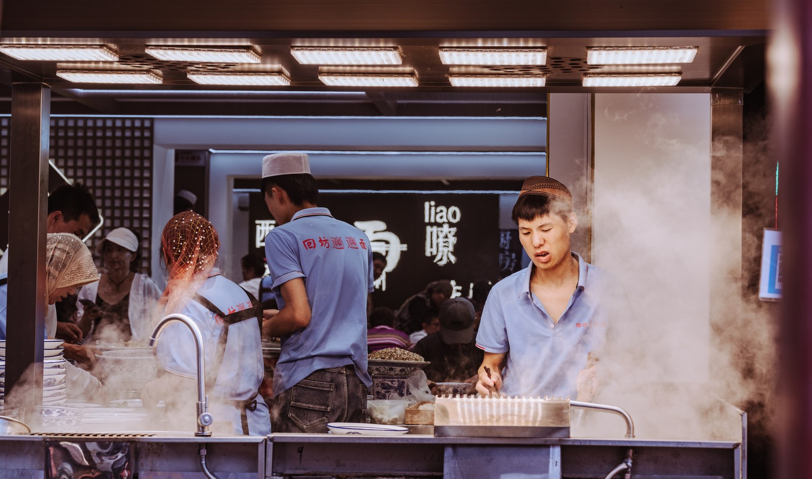 Workers face different directions across a counter divided by rising steam.
