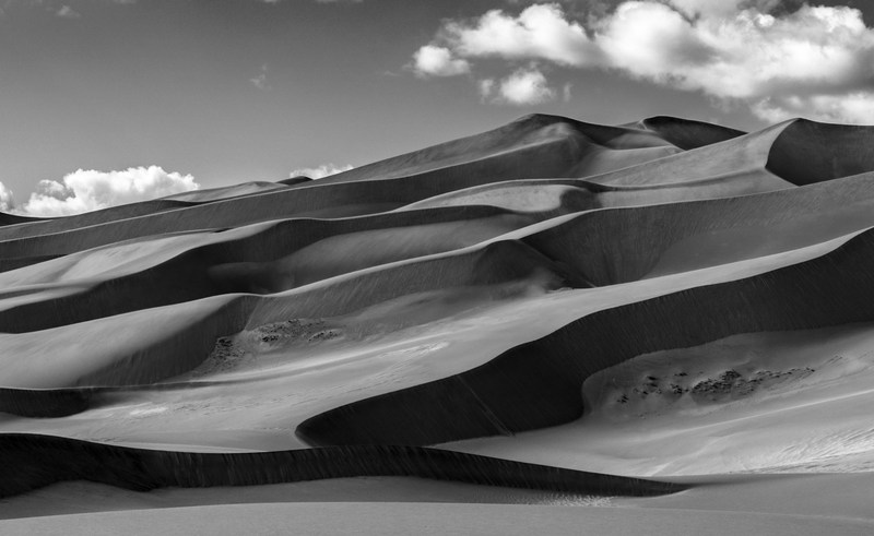 Monochrome dune ridges overlap beneath a few soft clouds.