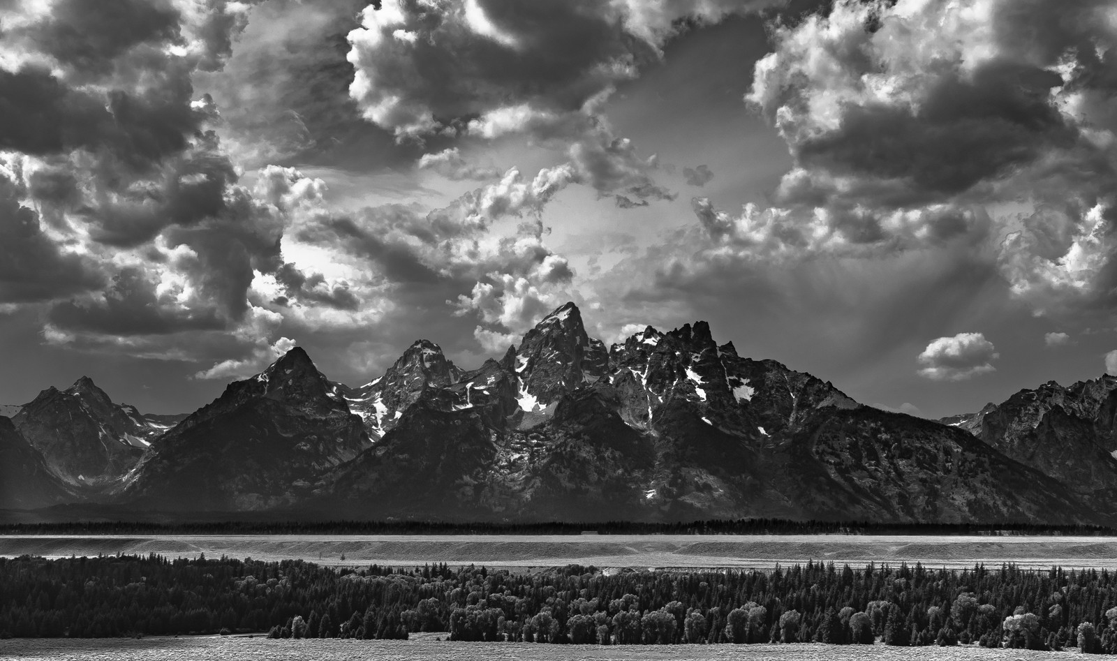 Dramatic clouds gather over the Teton Range above a valley.