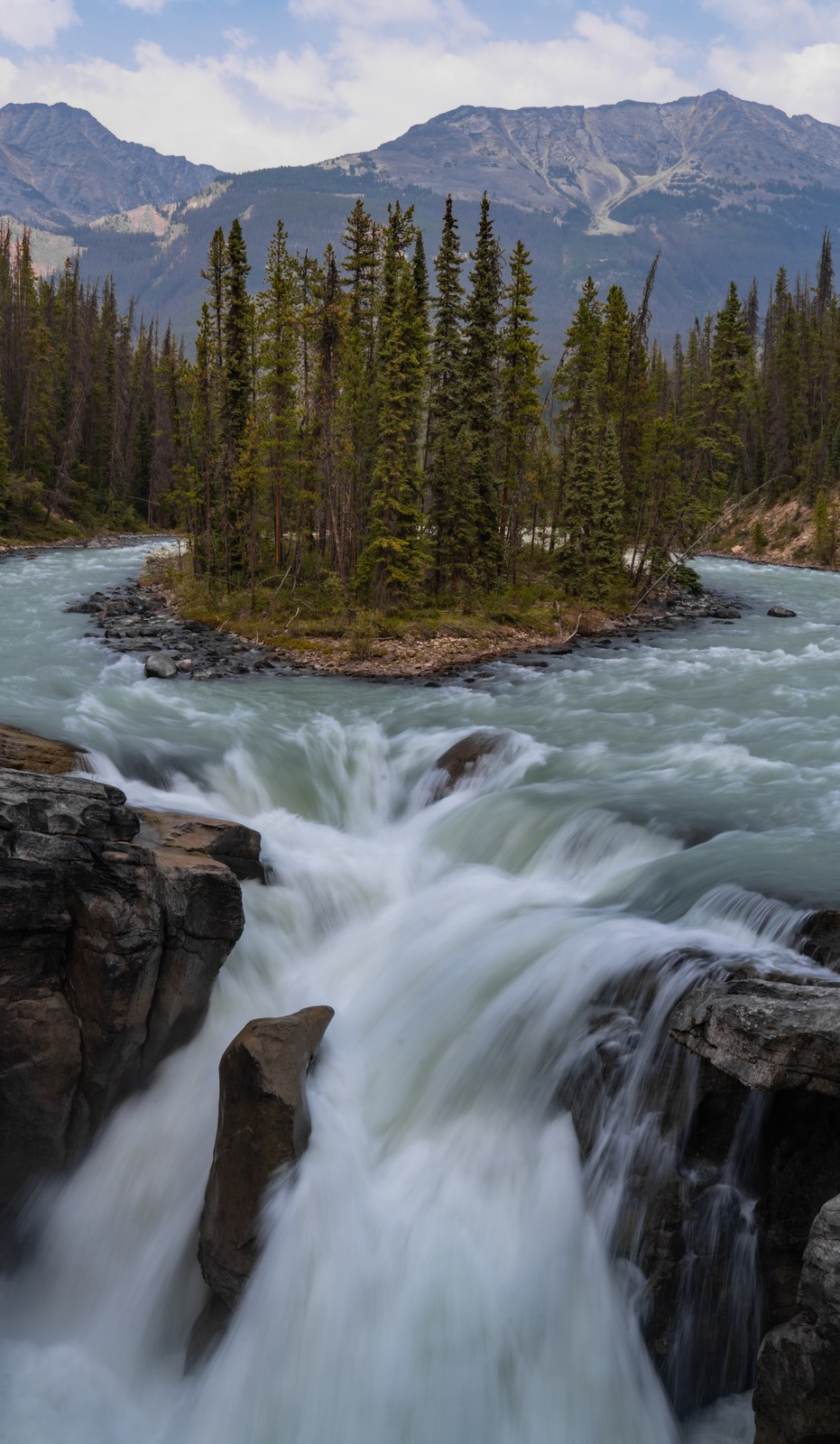 Water divides around a tree-covered island and converges above a foreground waterfall.