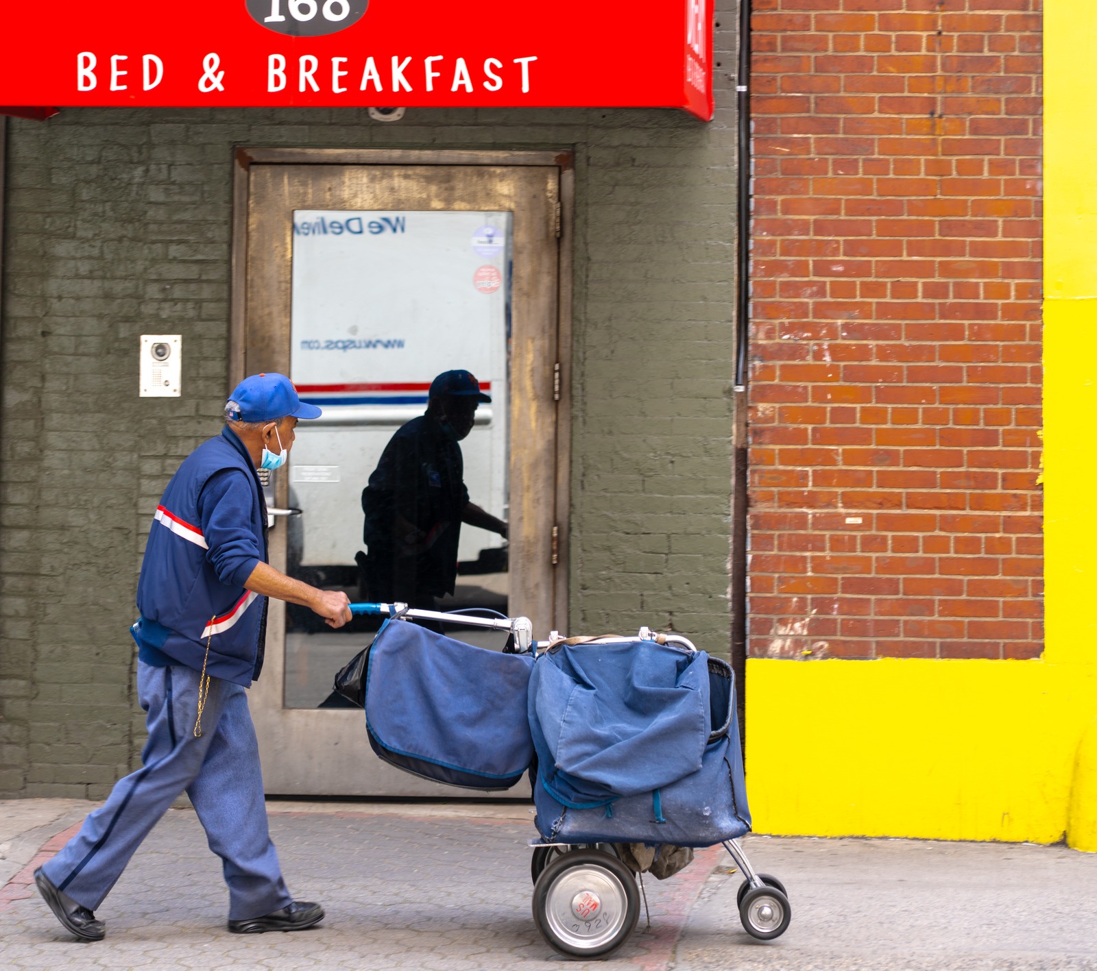 A person pushes a cart past a storefront door holding their reflection.