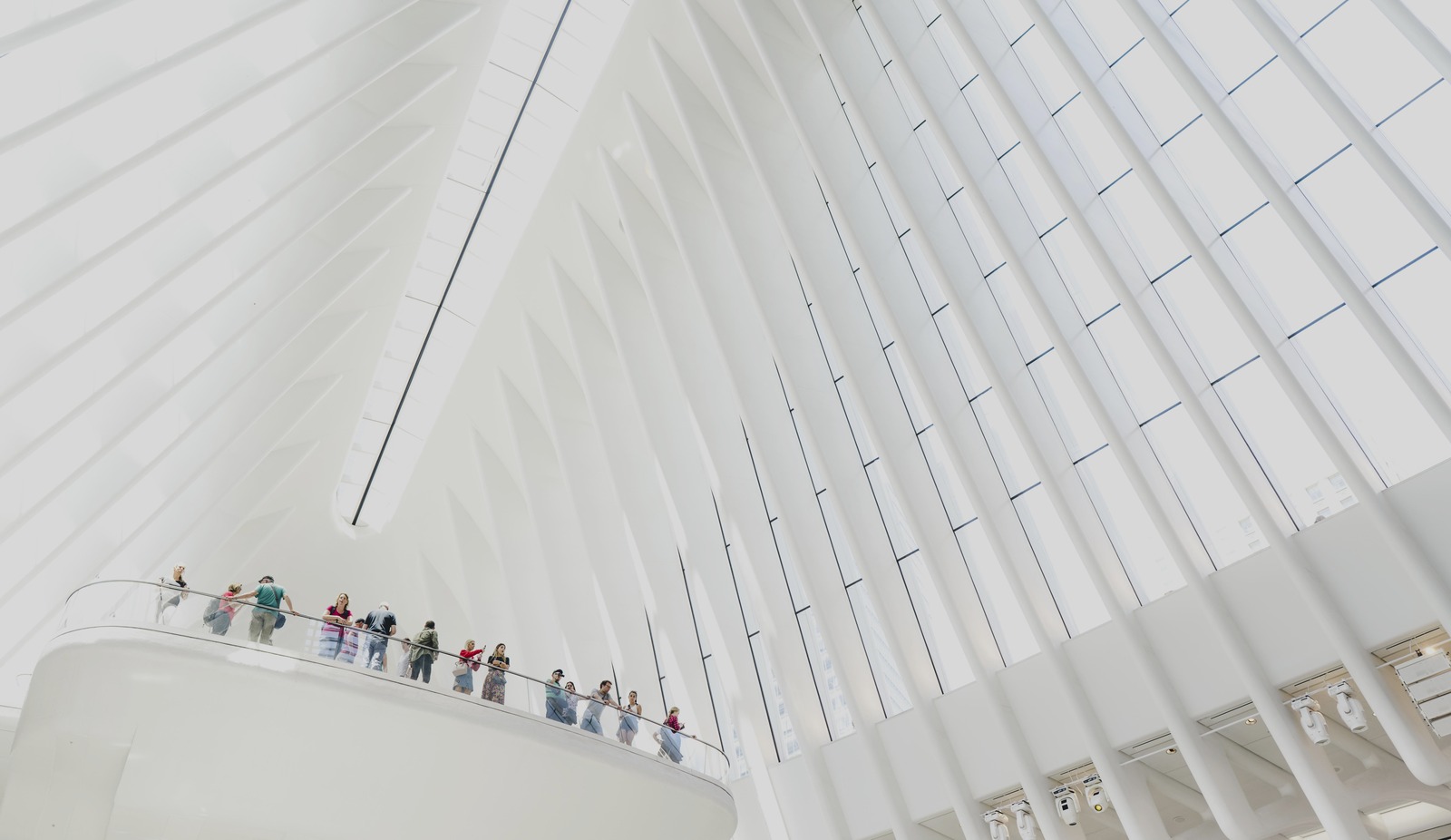 Small figures follow a balcony below sweeping white architectural ribs.