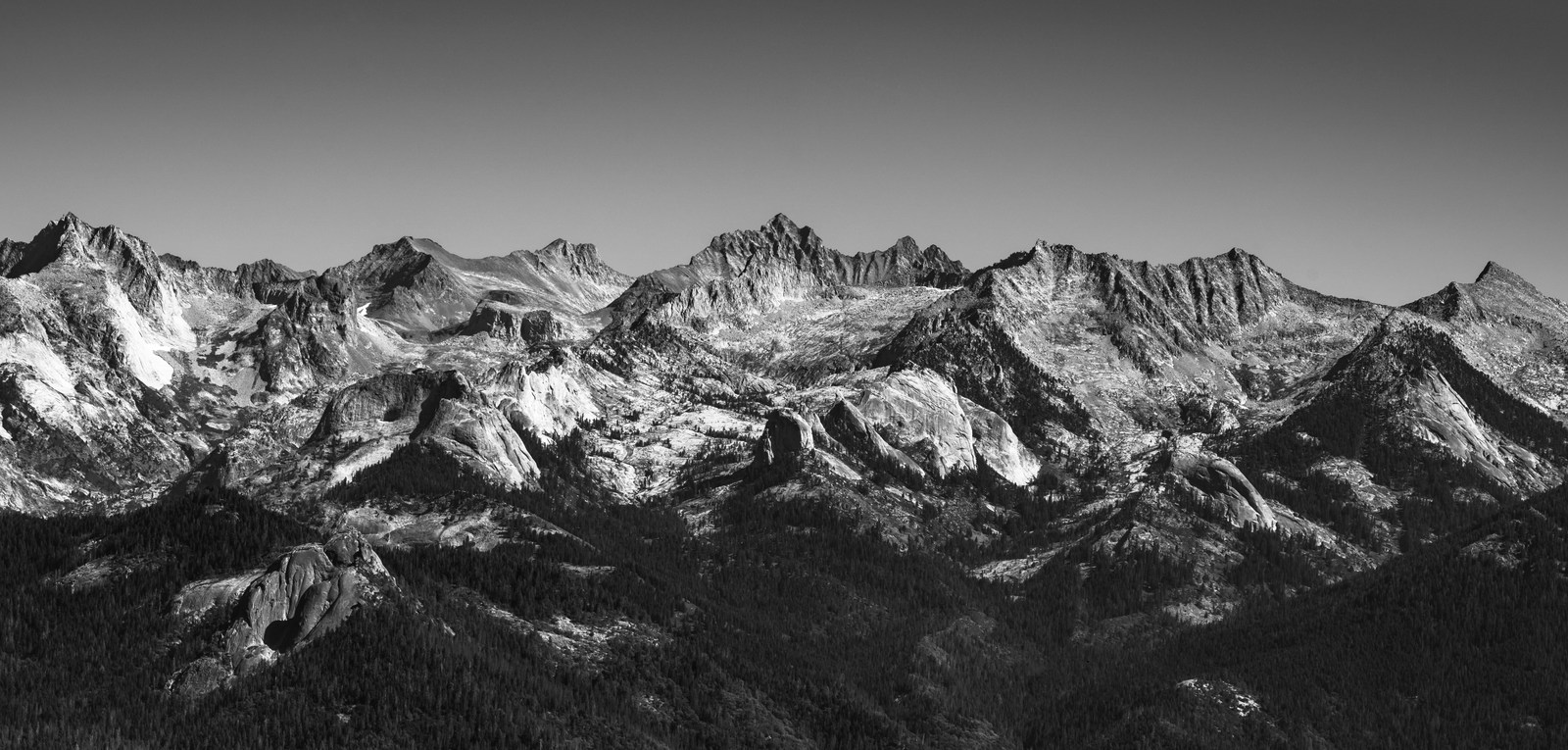 A black-and-white panorama shows serrated mountain ridges above dark forest.