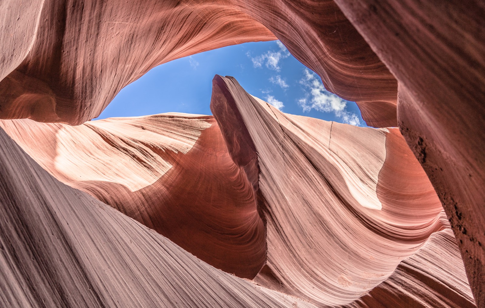 Striated sandstone curves around a blue opening of sky.