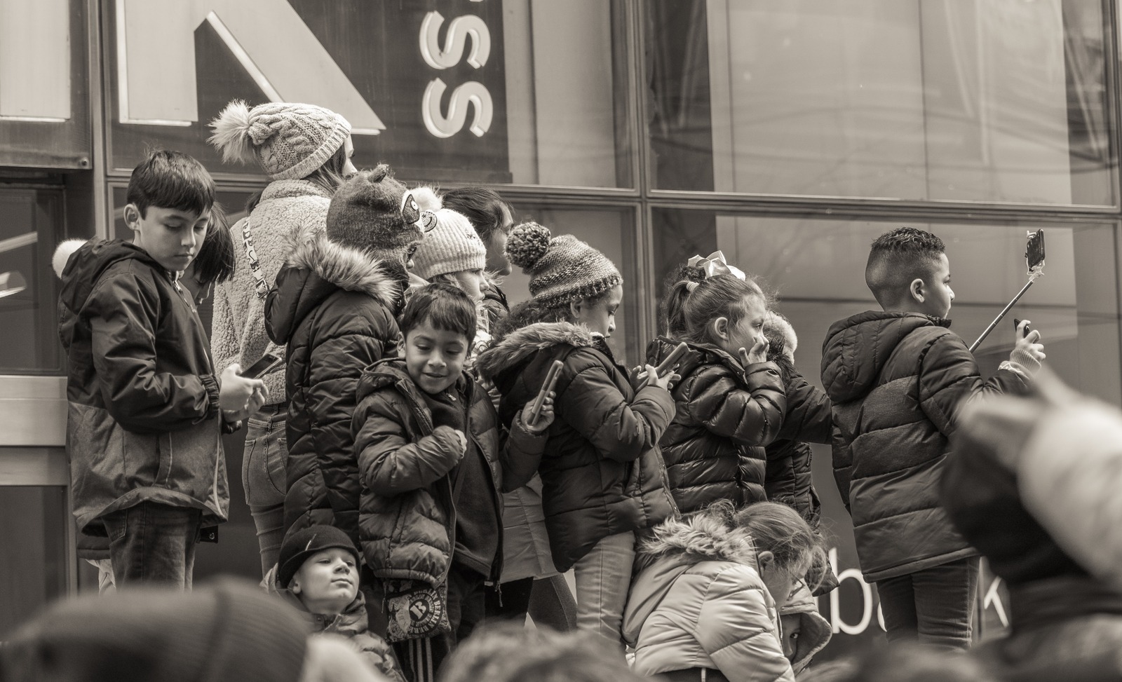 A group of children huddled together in the snow, one holding up a selfie stick
