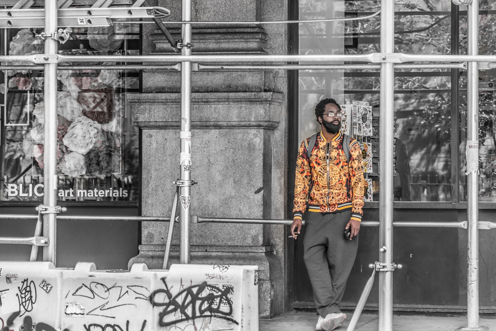 A man in a bright patterned jacket by scaffolding, the street in black and white.