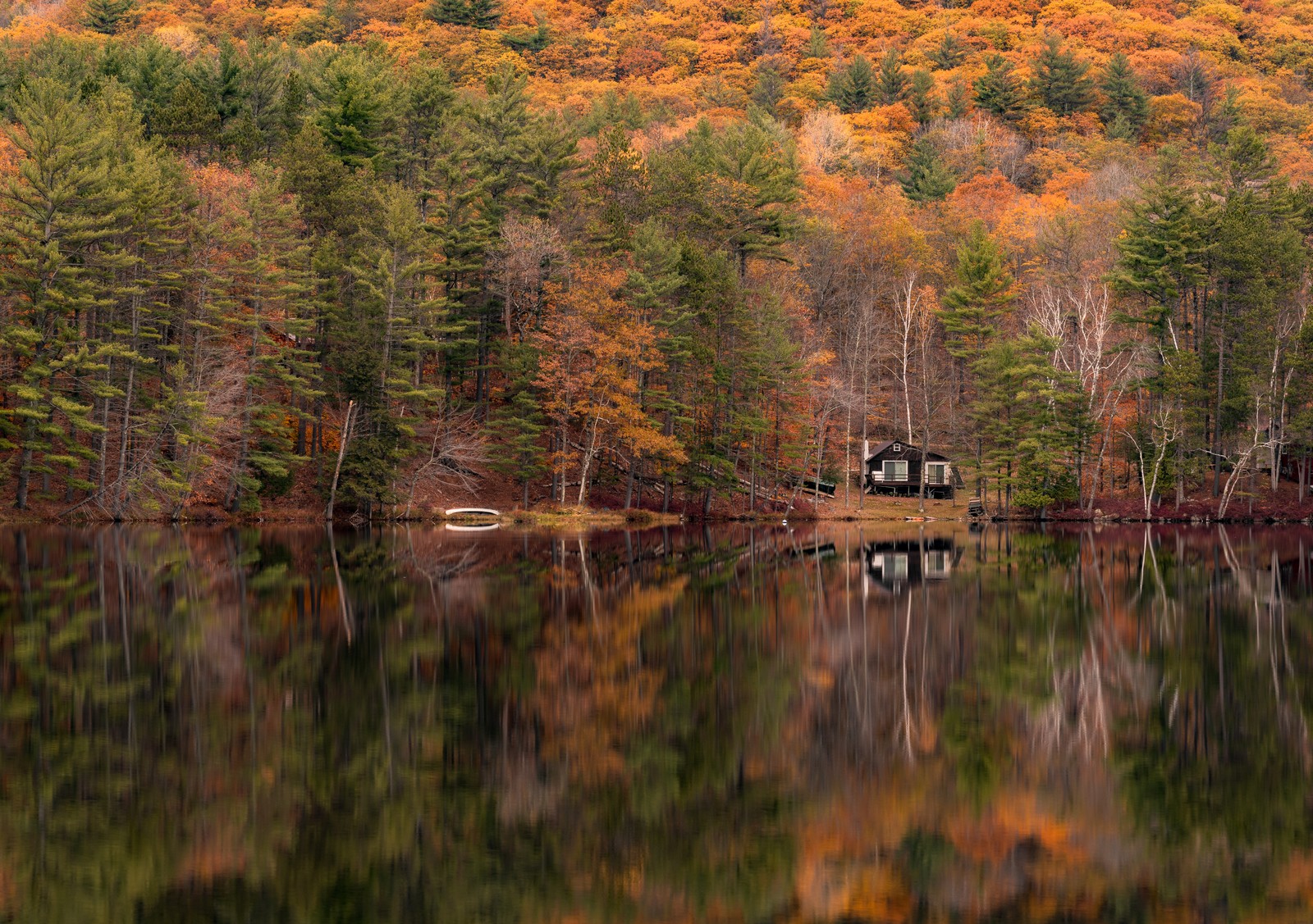A small cabin on the far shore of a still lake, autumn trees reflected.